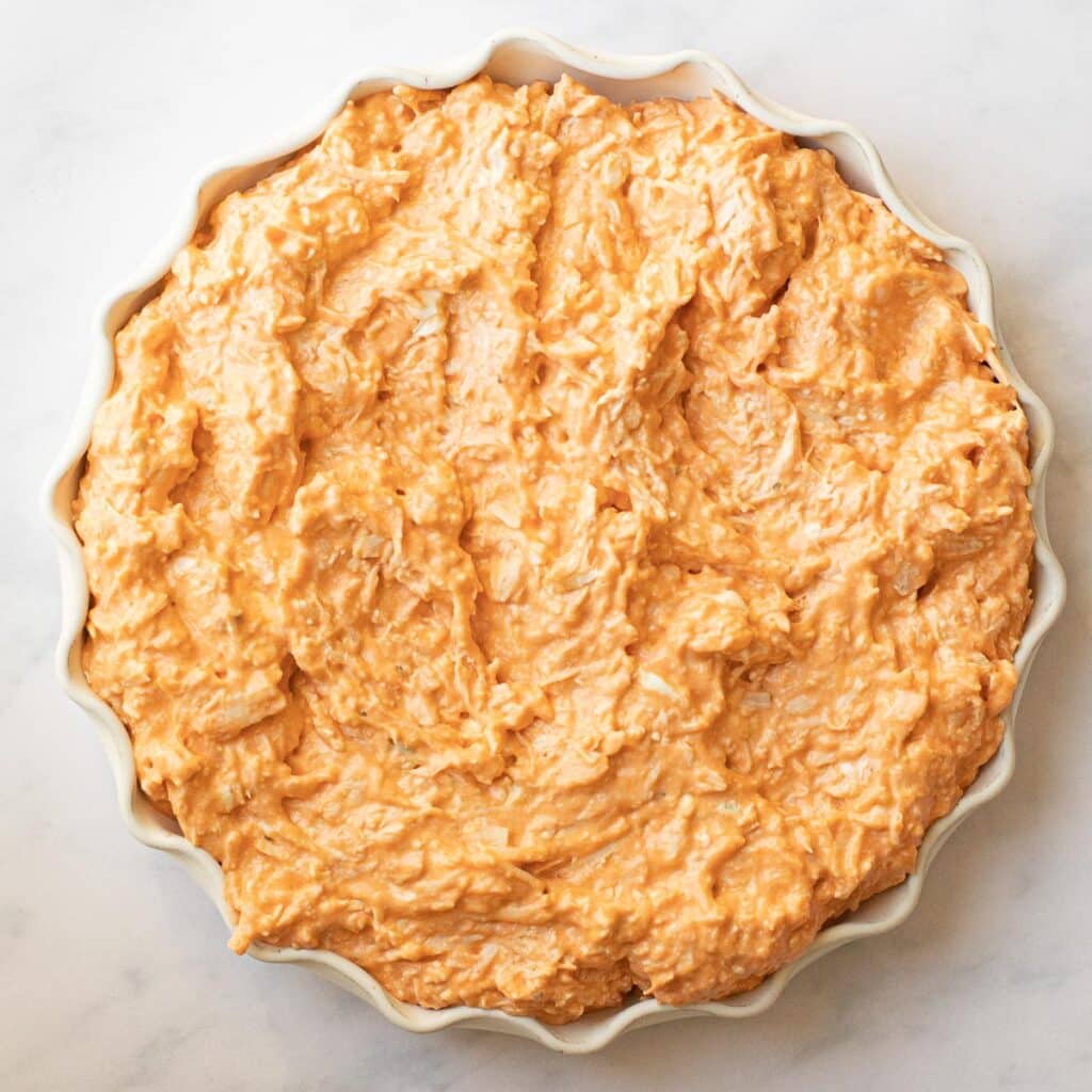 Uncooked buffalo chicken dip spread in a pie plate