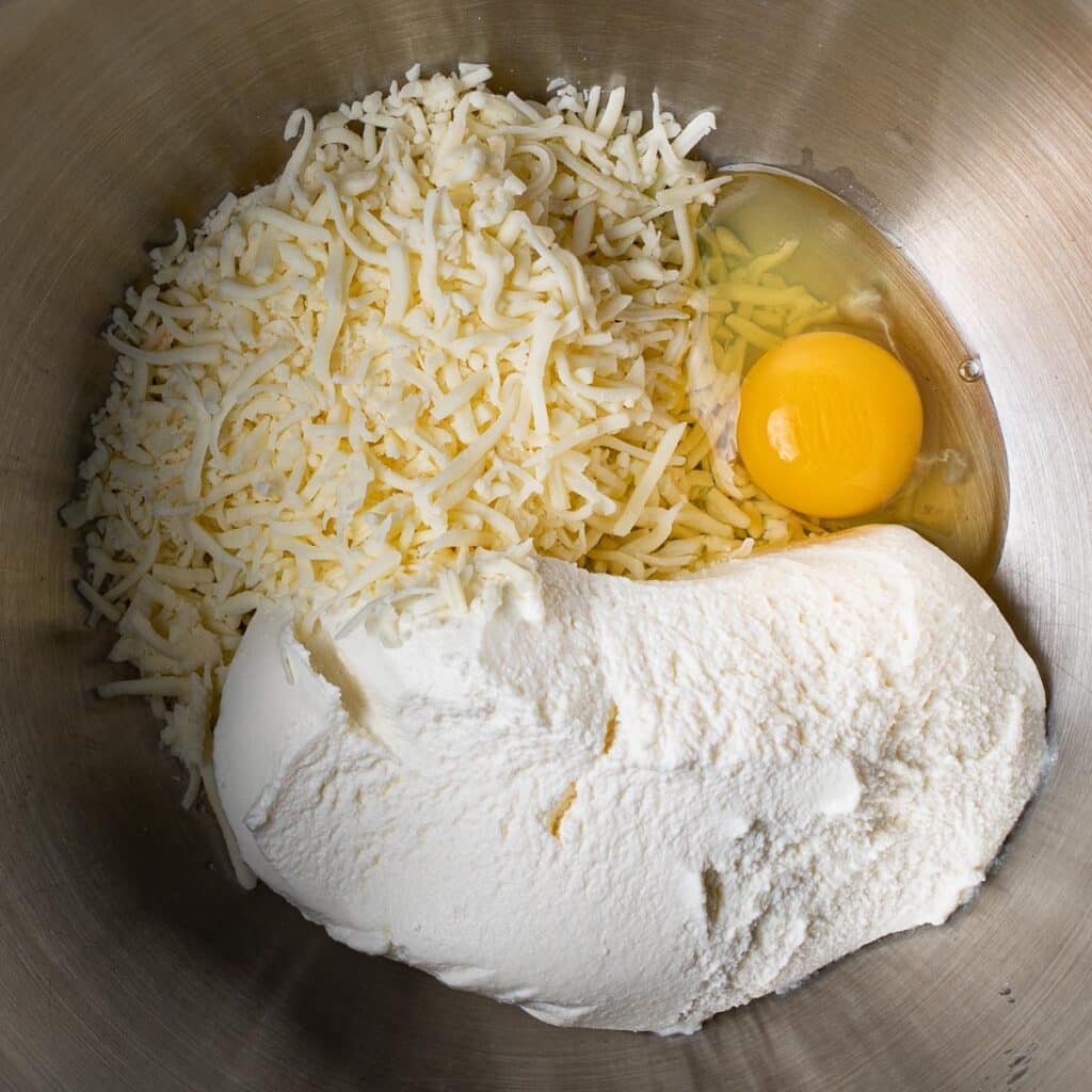 Ricotta cheese, mozzarella cheese and an egg in a stainless steel mixing bowl