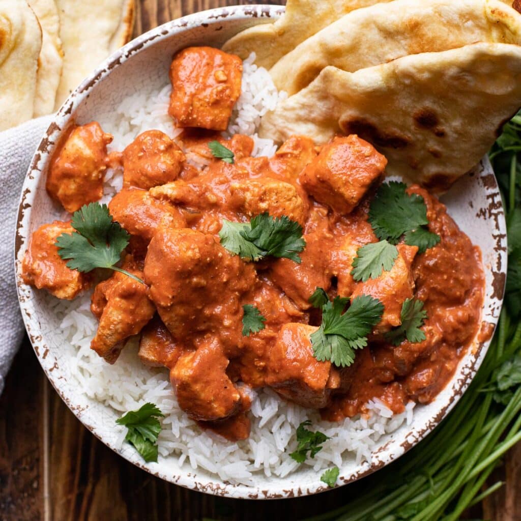 A white bowl with chicken tikka masald over white rice with naan