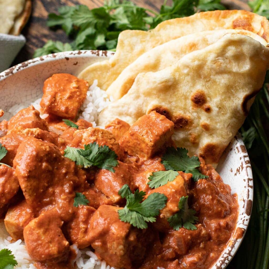 Naan bread dipped in a bowl of chicken tikka masala