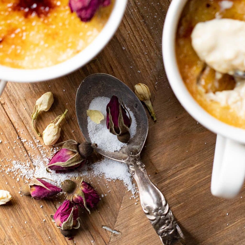 An antique spoon with sugar and dried rose buds on a wooden board