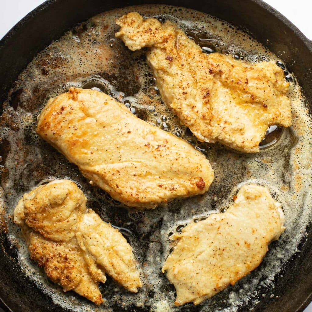 champagne chicken cooking in melted butter in a large pan