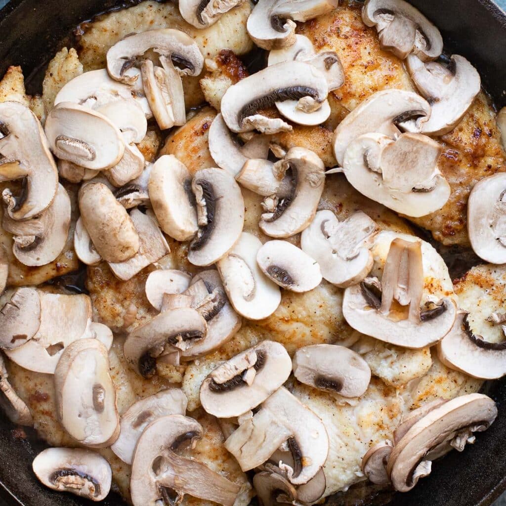 sliced mushrooms and chicken cooking in a pan