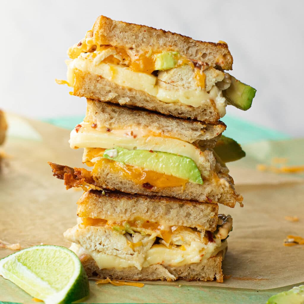 Halves of grilled chicken and avocado sandwiches stacked on top of each other