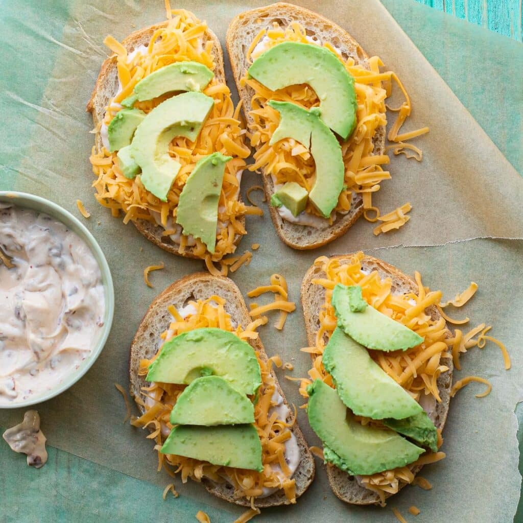 Avocado slices and grated cheddar cheese on top of four slices of bread