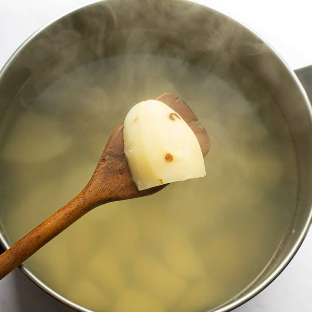 A piece of potato on a wooden spoon over a pot of boiling potatoes