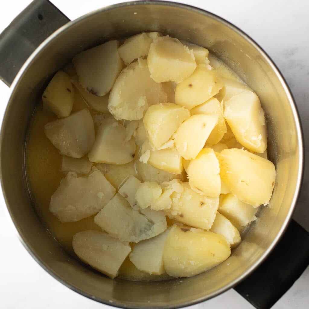 Cooked potatoes in a large stockpot with melted butter