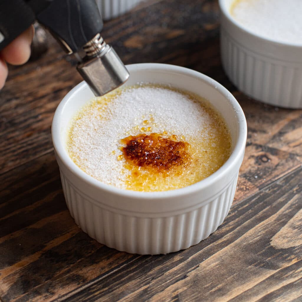 A kitchen butane torch burning the top of creme brulee.