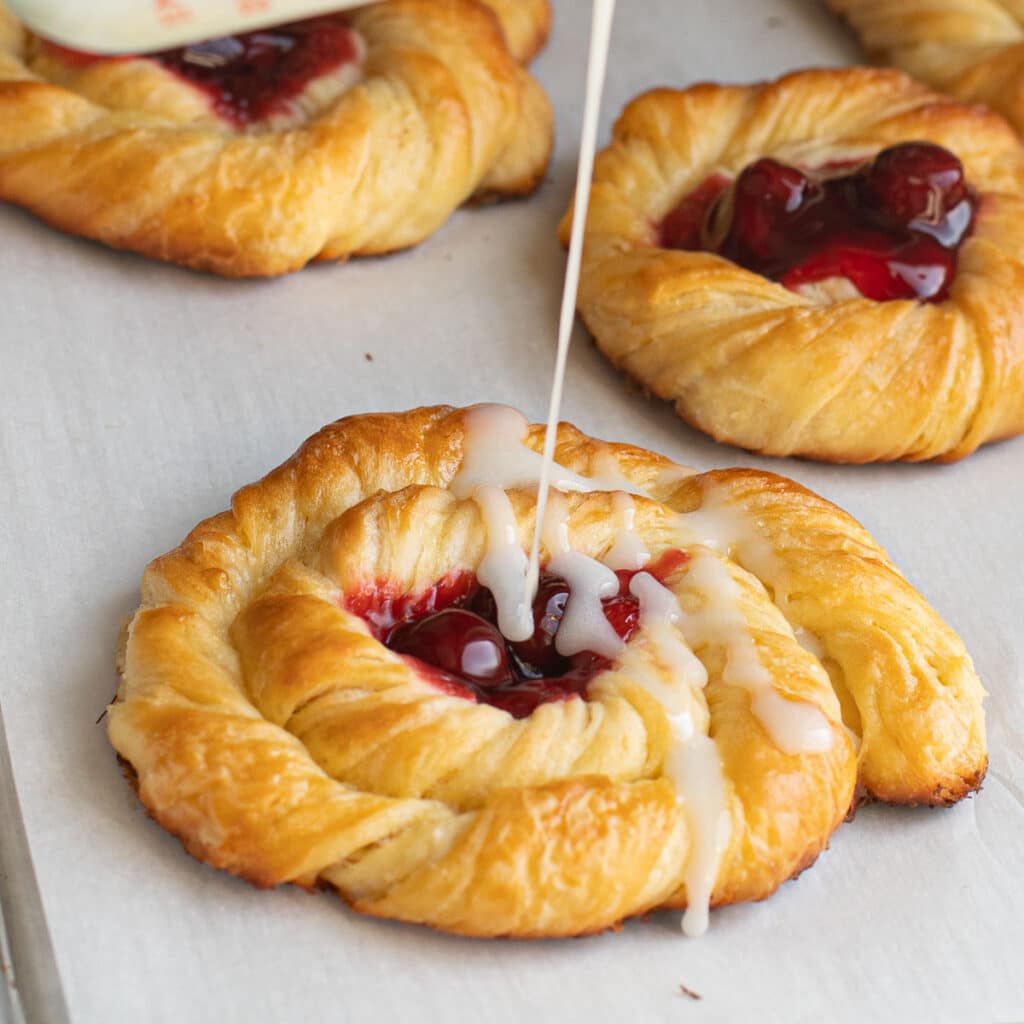 A homemade cherry danish being drizzle with white glaze