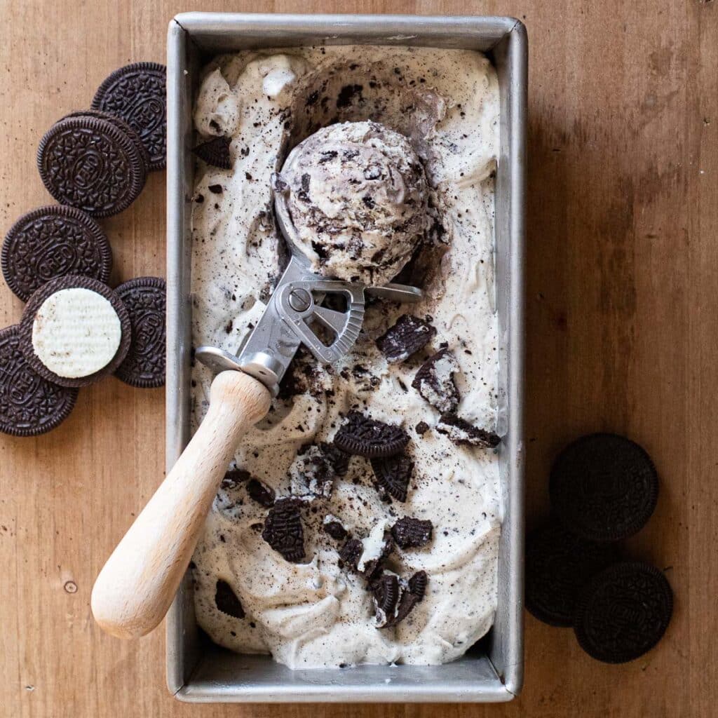 No churn Oreo ice cream in a silver loaf pan with an ice cream scooper