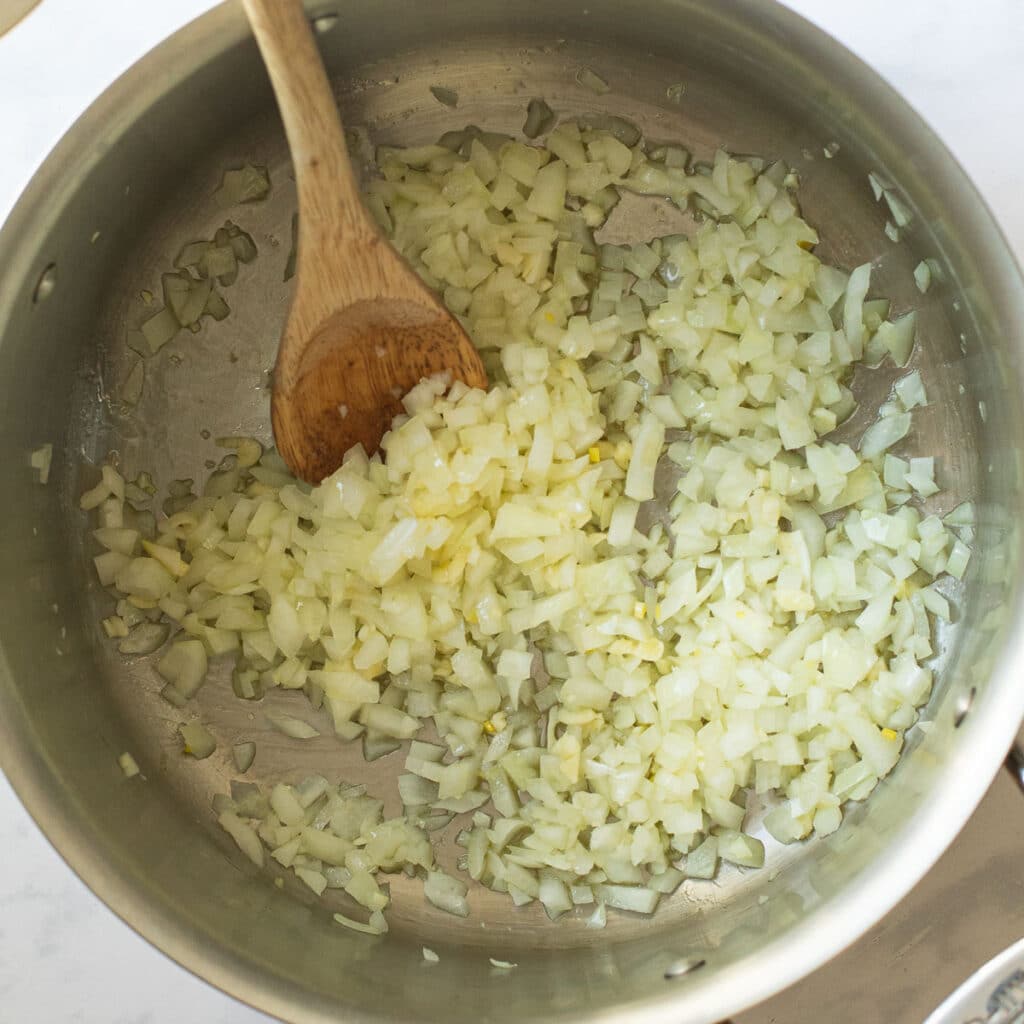 Diced onions and garlic cooking in a stainless steel pot