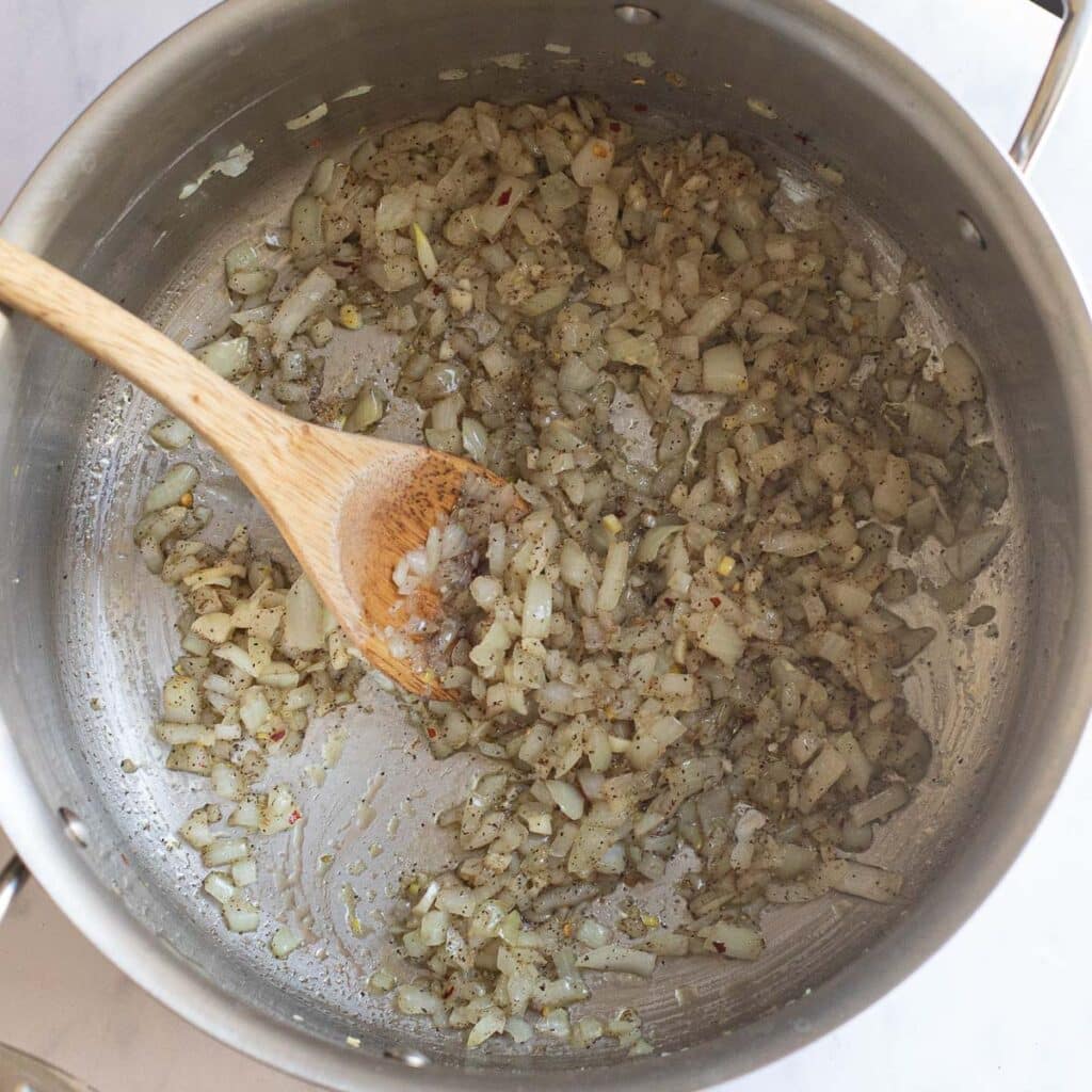 Diced onions, garlic, pepper, and other seasonings cooking in a stainless steel pot
