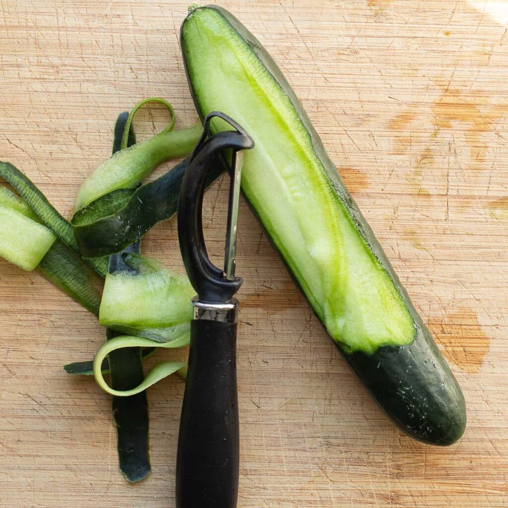 A cucumber being cut into ribbons with a vegetable peeler