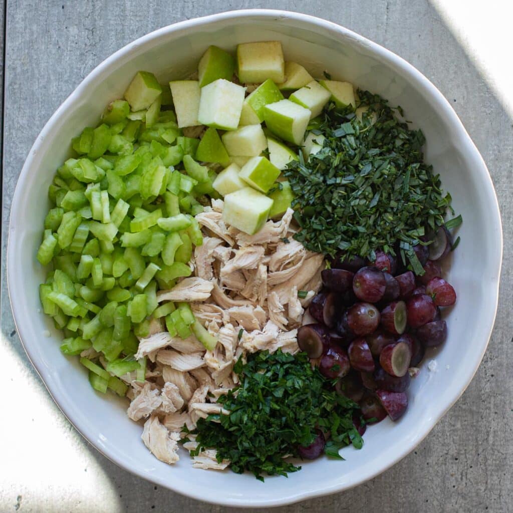 Red grapes, green apples, fresh tarragon, chopped celery and shredded chicken in a white bowl