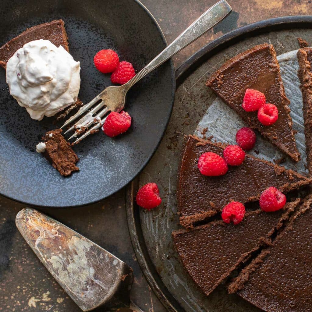 flourless chocolate cake on a black plate with a silver fork and raspberries