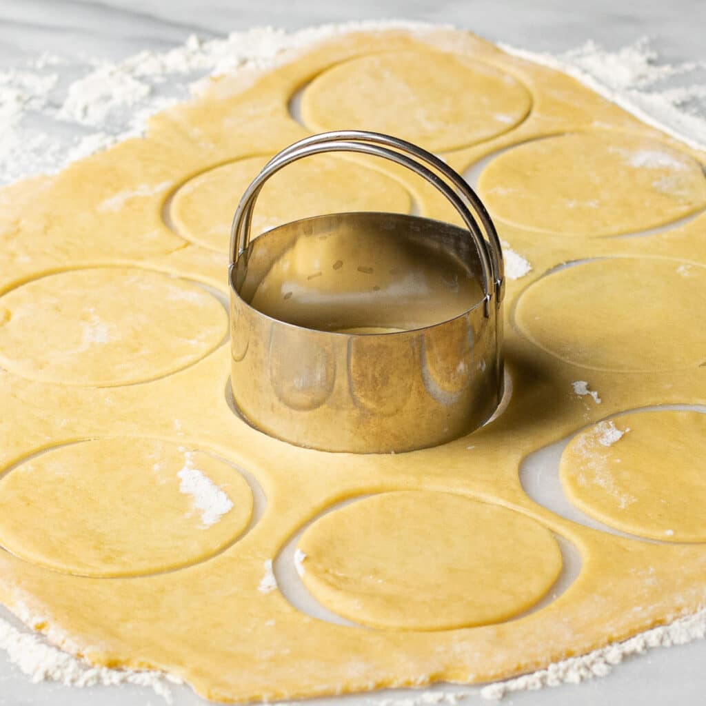 A silver biscuit cutter making circles in cookie dough