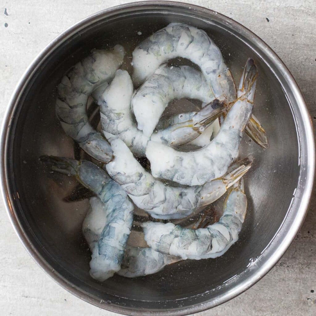 Raw shrimp in a silver bowl full of ice water