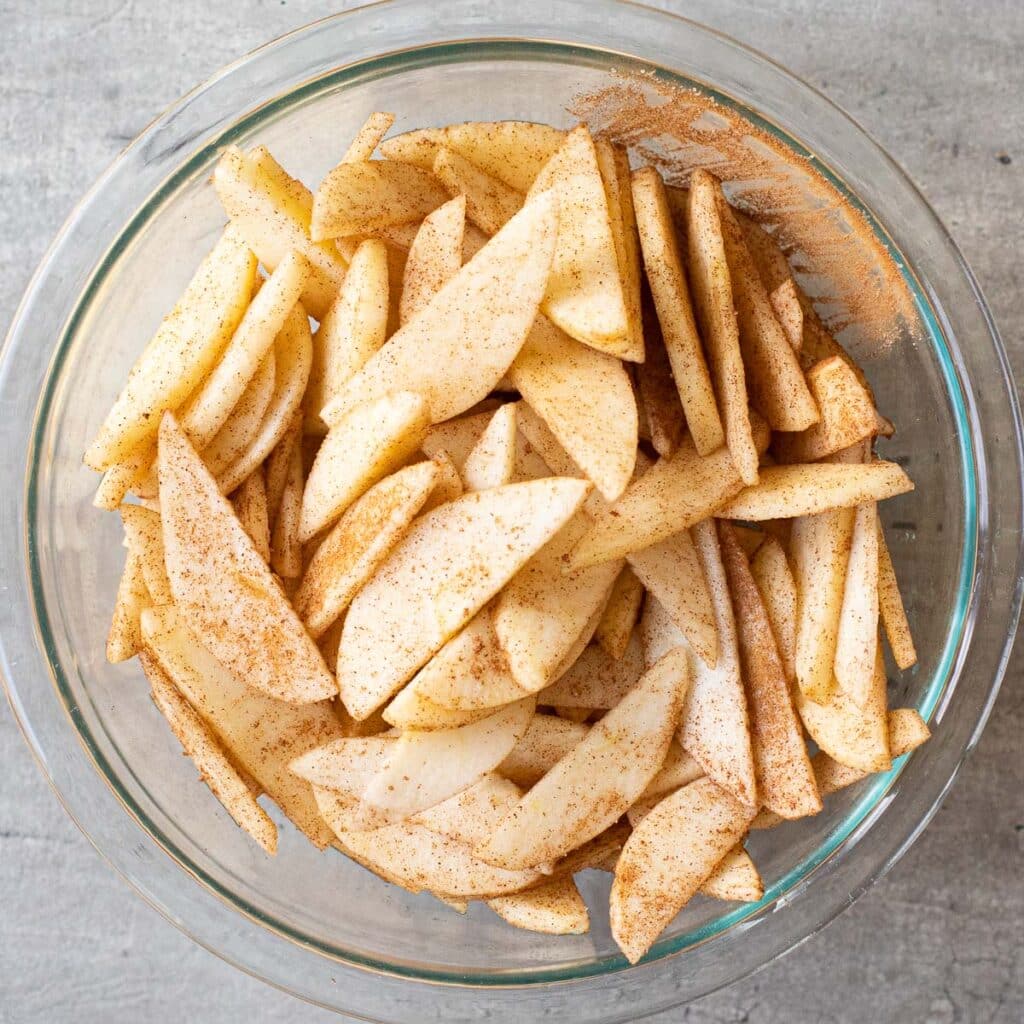Sliced apples tossed in cinnamon and sugar in a glass bowl