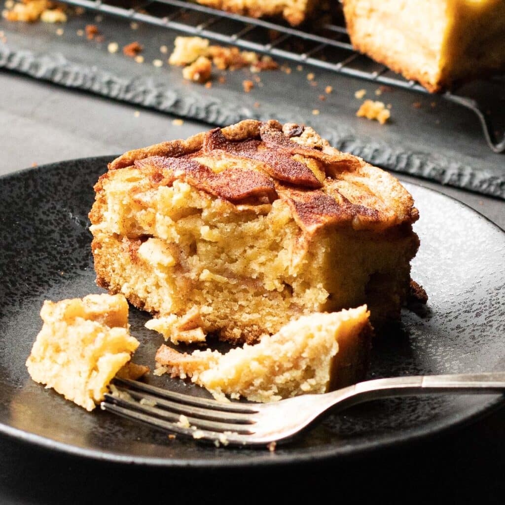 A piece of Passover apple cake on a black plate with a silver fork