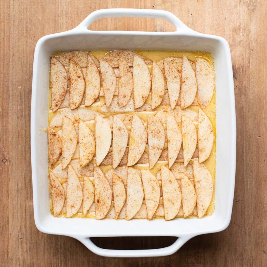 Apple slices arranged over cake batter in a white square baking dish