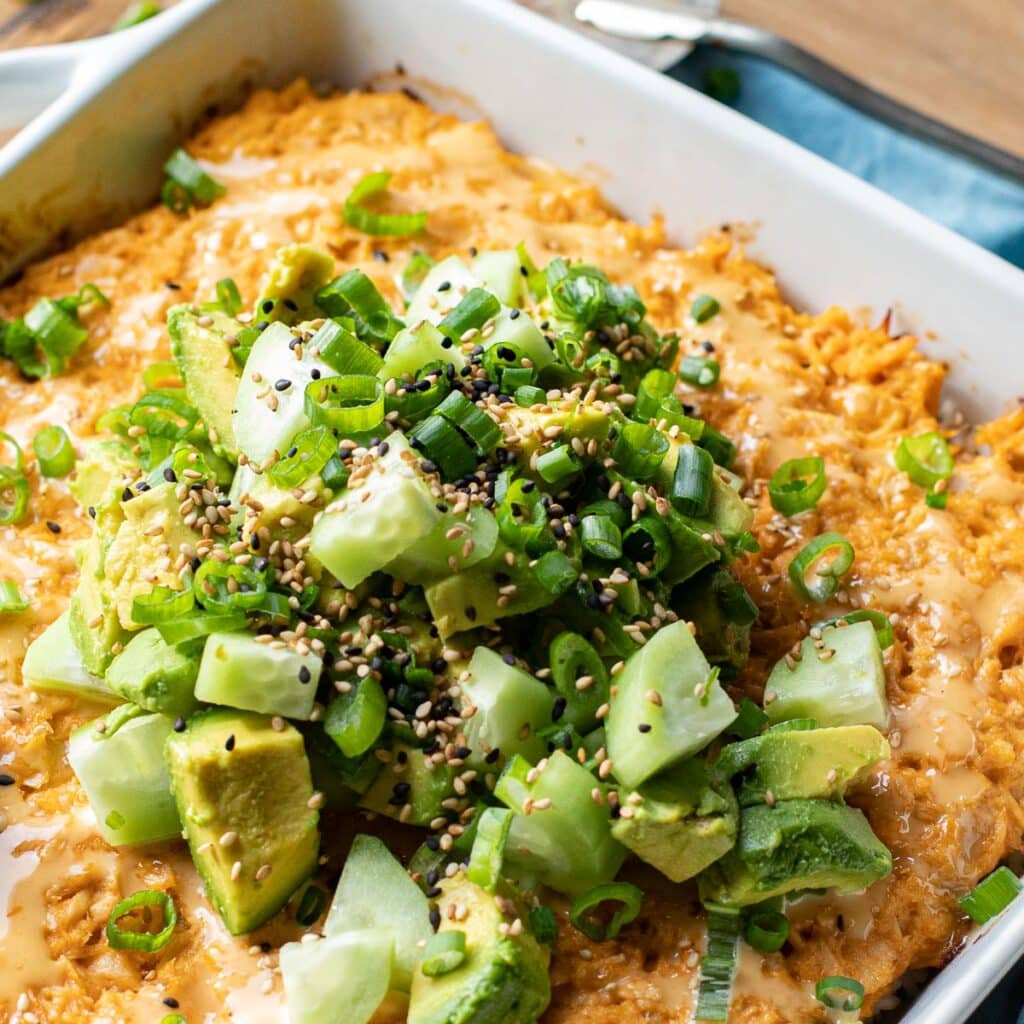 Sushi bake recipe with spicy tuna topped with diced avocados and cucumbers, scallions and sesame seeds