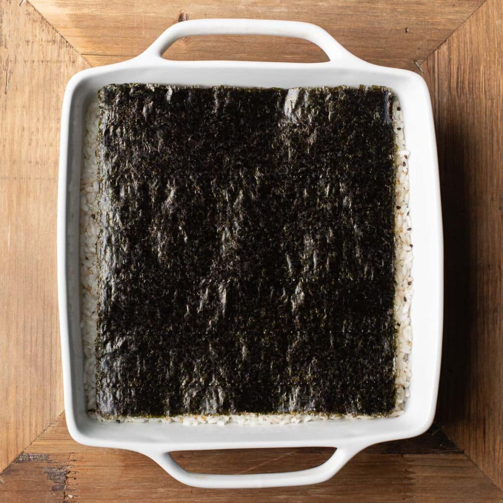 Nori sheets on top of sushi rice in a white square casserole dish