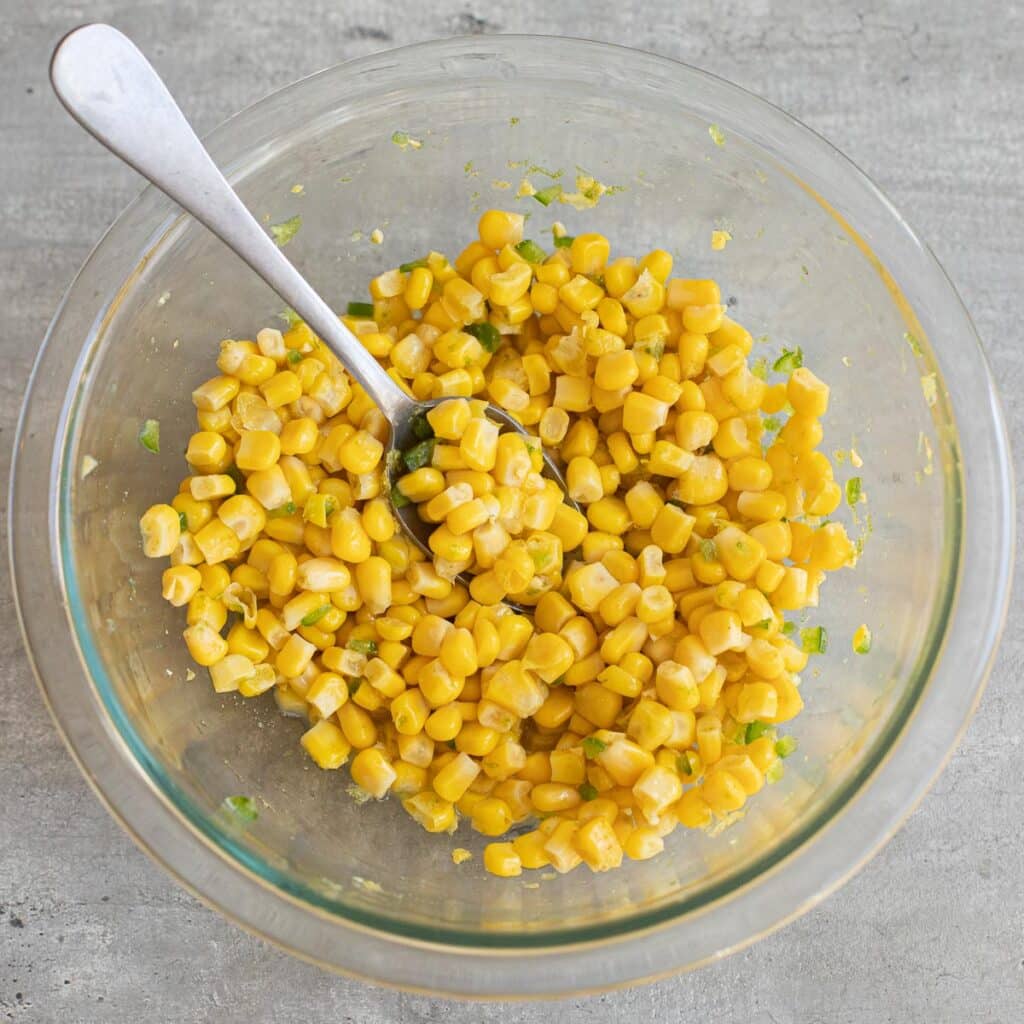 corn and diced jalapeno peppers in a glass mixing bowl