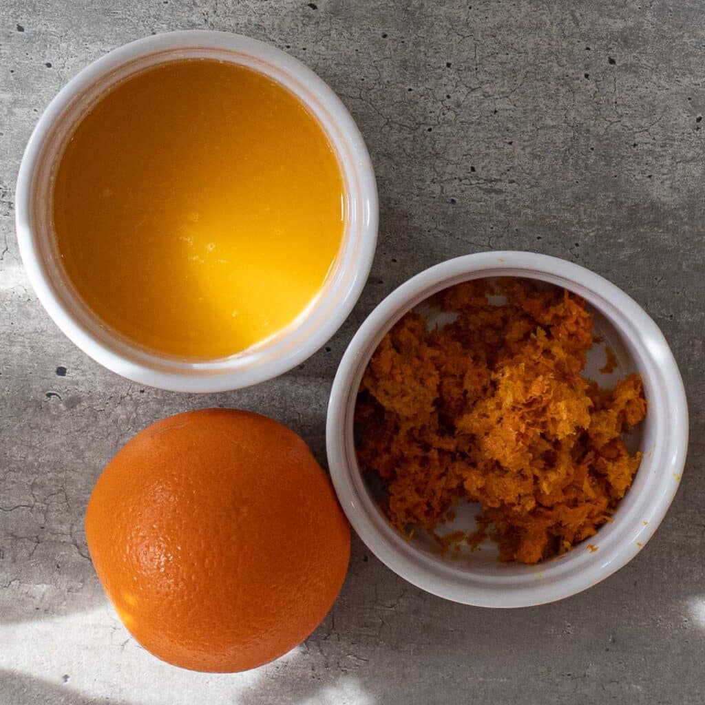 Fresh orange juice and orange zest in small white bowls