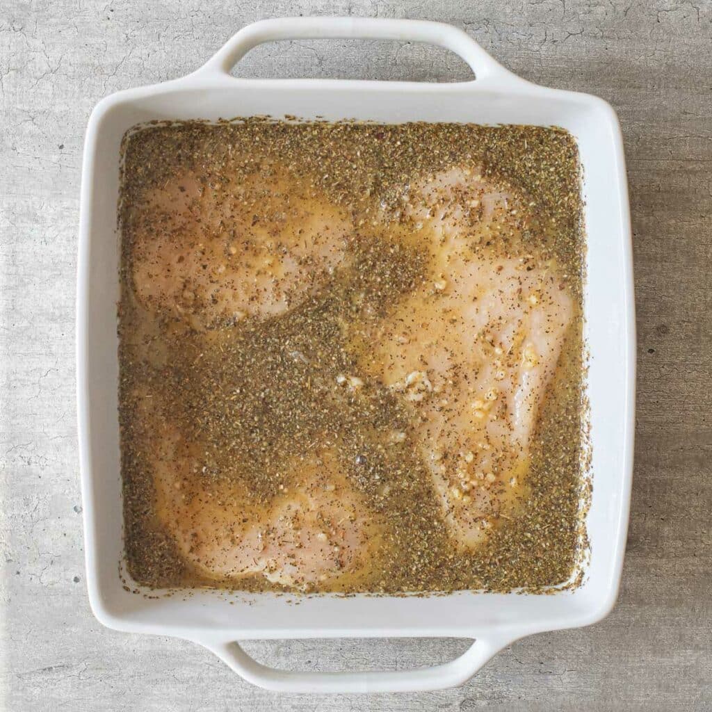 chicken marinating in taco seasoning in a white baking dish