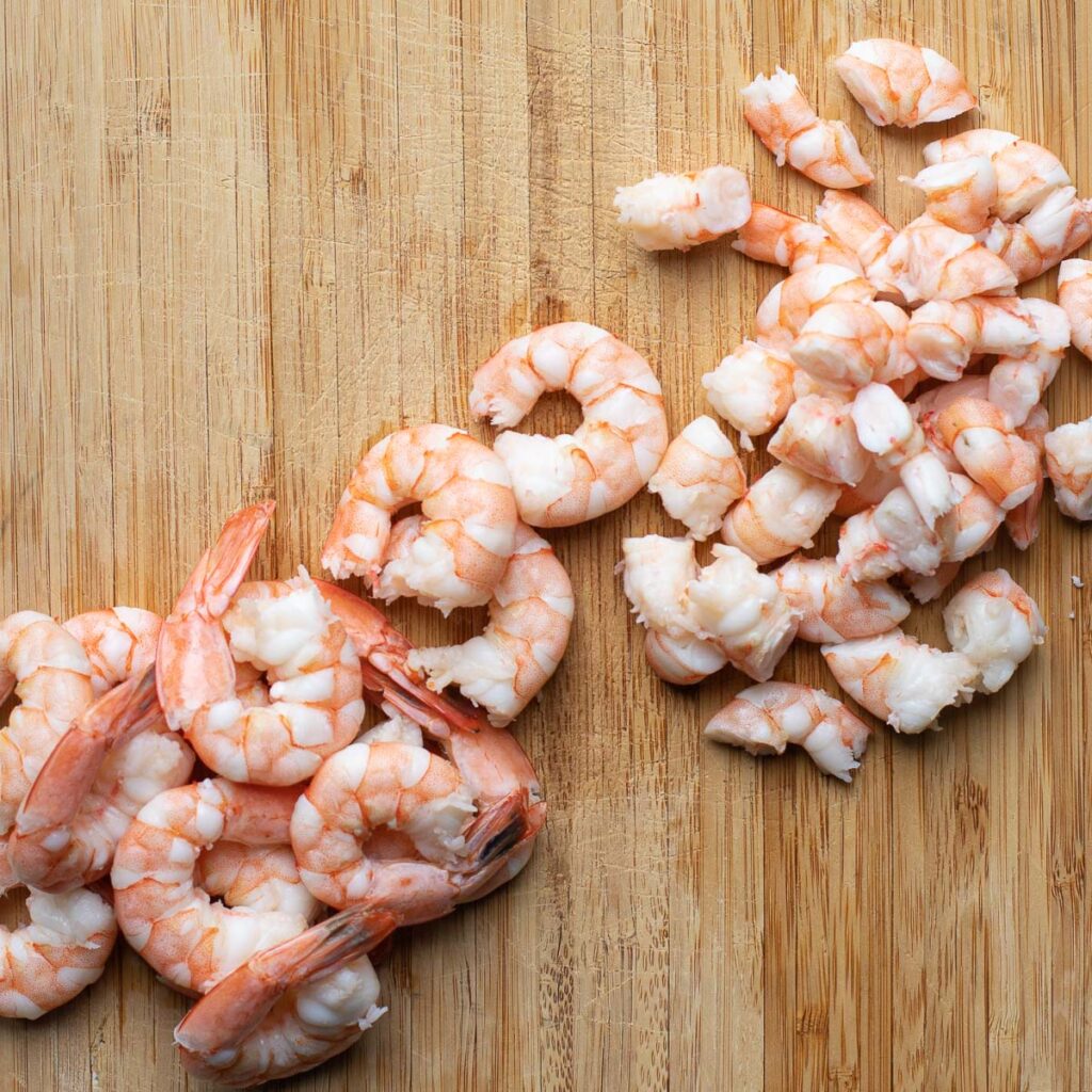 cooked shrimp chopped into pieces on a wooden cutting board