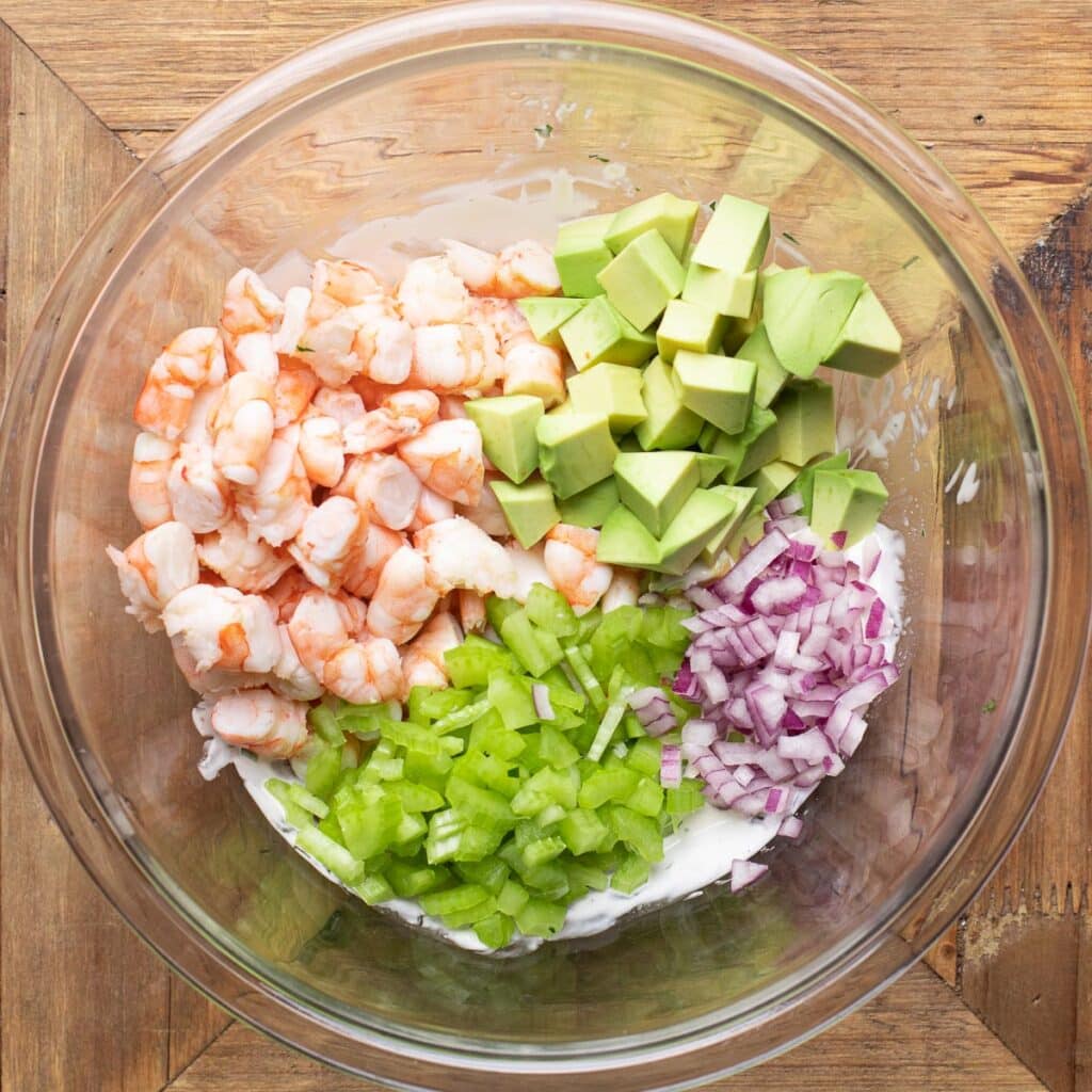 chopped shrimp, diced avocado, diced red onion and chopped celery in a glass mixing bowl