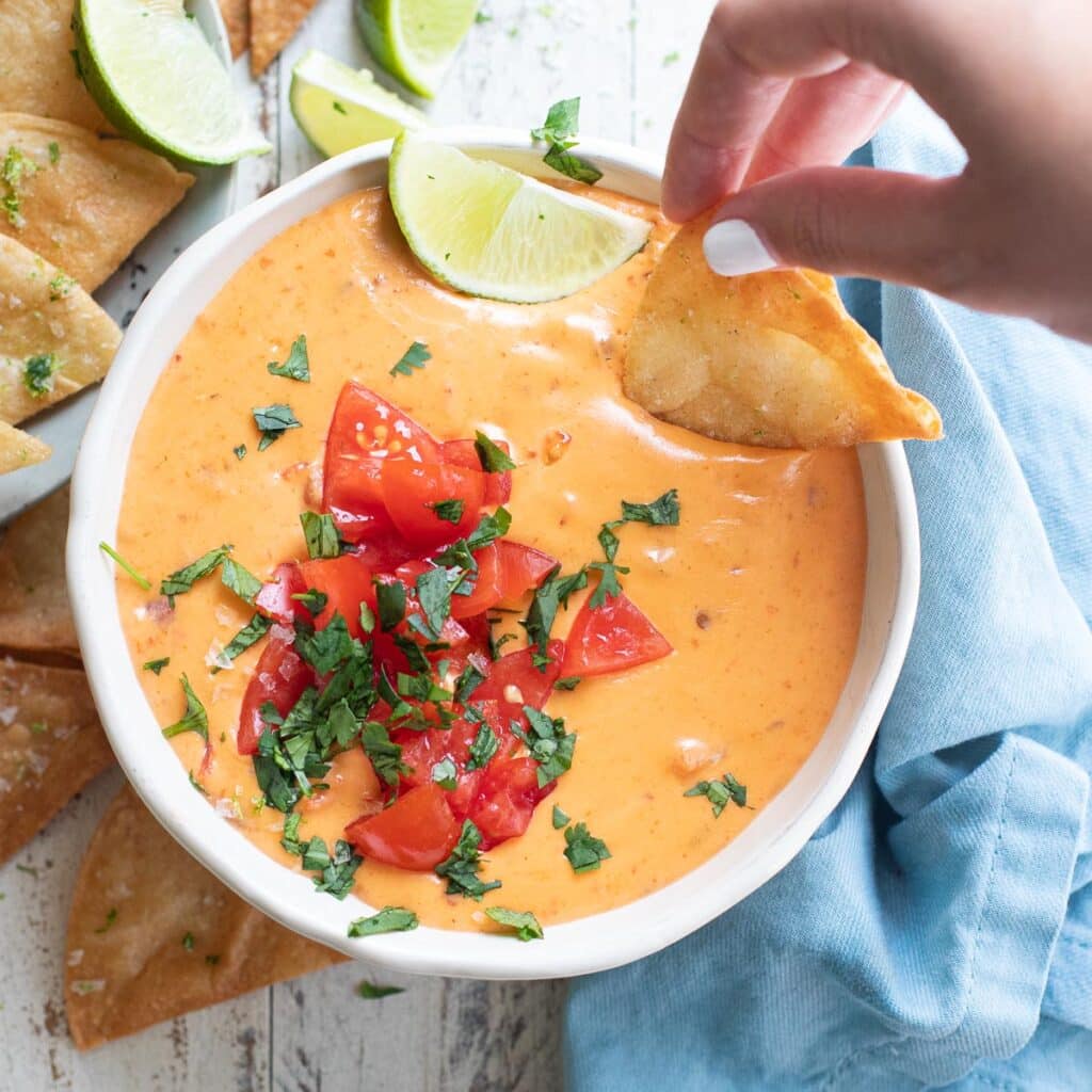 A hand dipping a chip into queso dip