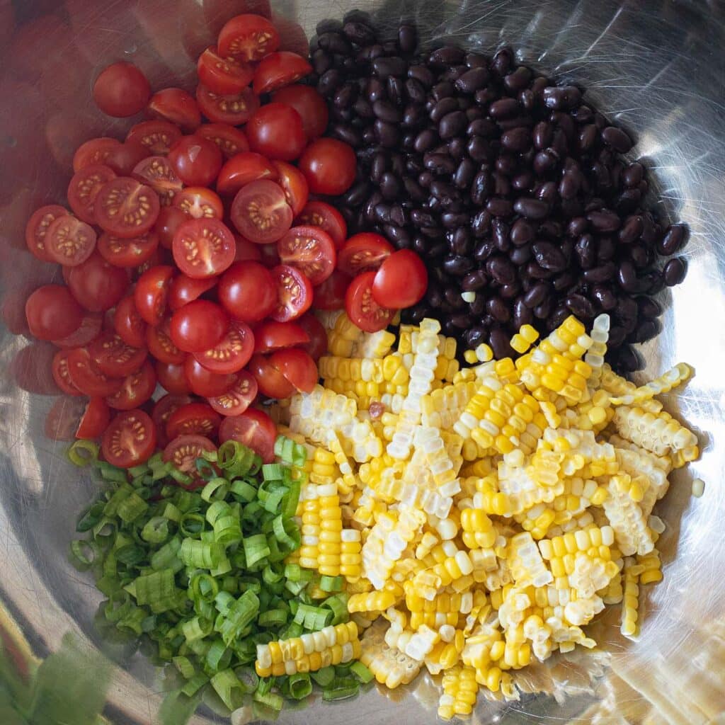 black beans, corn, scallions and cherry tomatoes in a silver mixing bowl