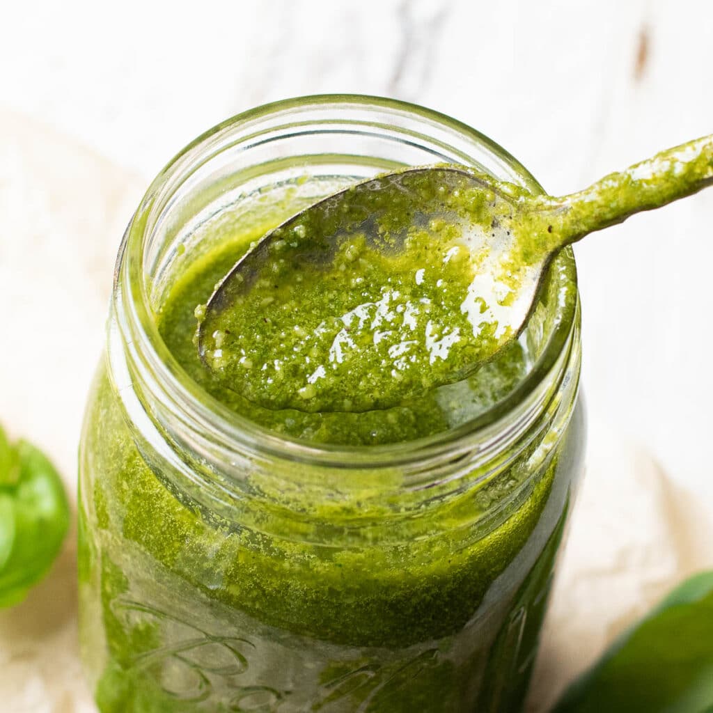 a spoon dipped into a jar of pesto sauce