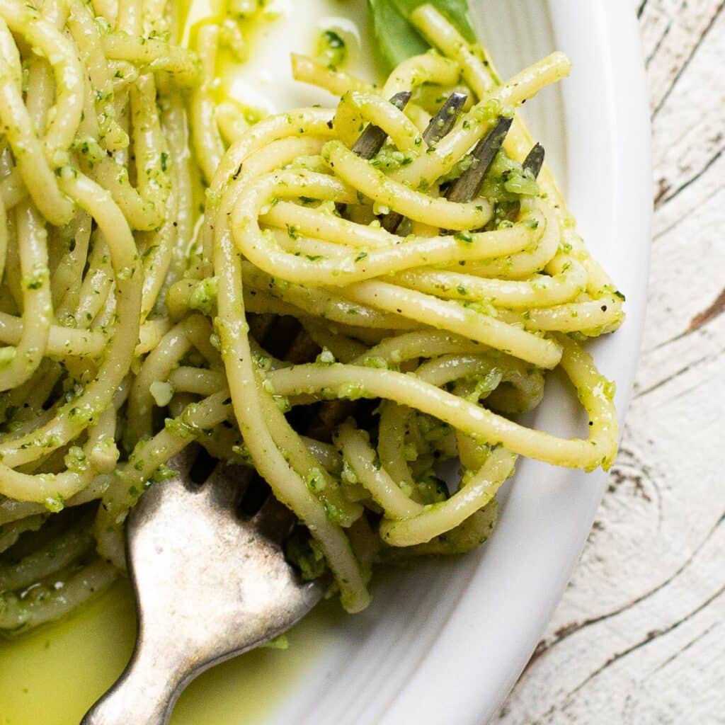 a forkful of spaghetti on a white plate with green sauce