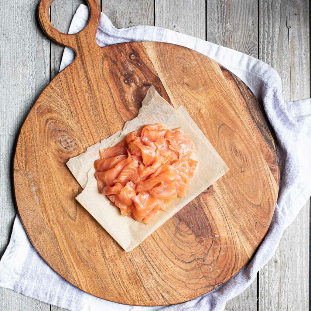 smoked salmon in a pile in the center of a round wooden serving board