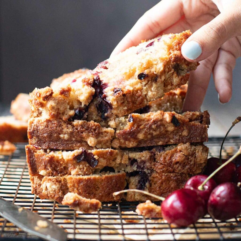 homemade cherry bread slices, stacked up, with a hand reaching for a piece