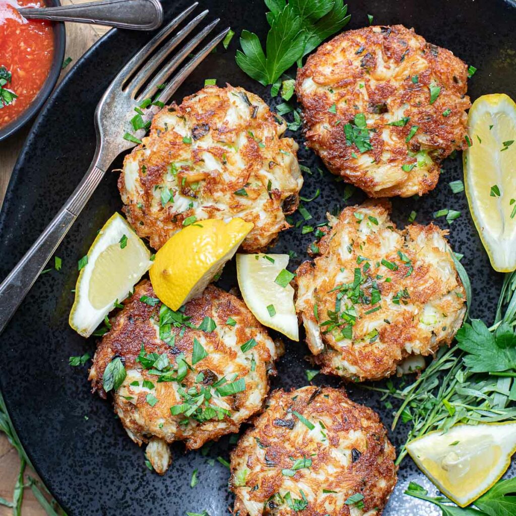 crab cakes on a black plate with lemon wedges and fresh parsley