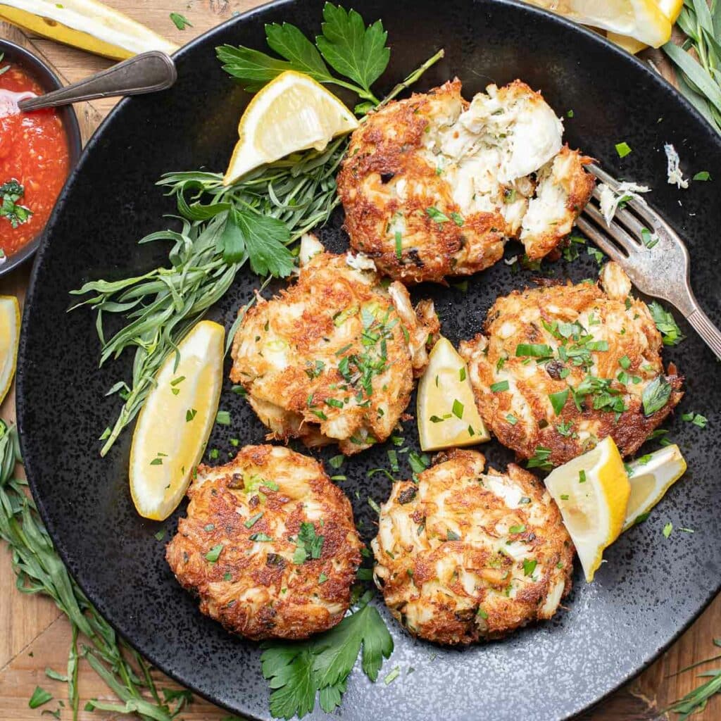 a plate of crab cakes with fresh tarragon and lemon wedges