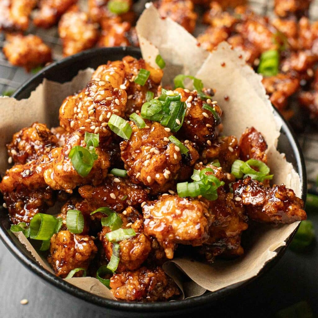 a bowl of Korean fried chicken garnished with sesame seeds and chopped scallions