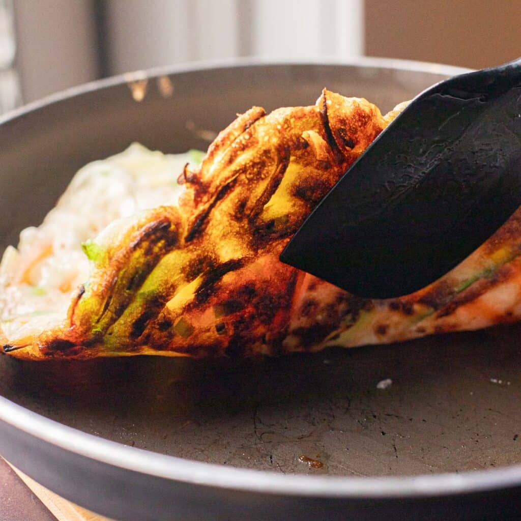 A spatula flipping a Korean vegetable pancake in a pan