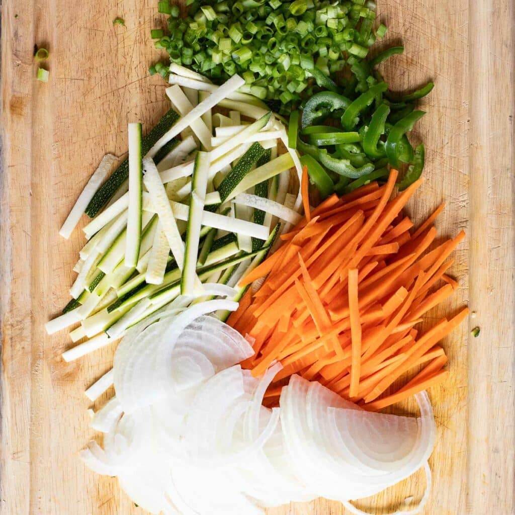 chopped carrots, zucchini, scallions and onions on a wooden cutting board