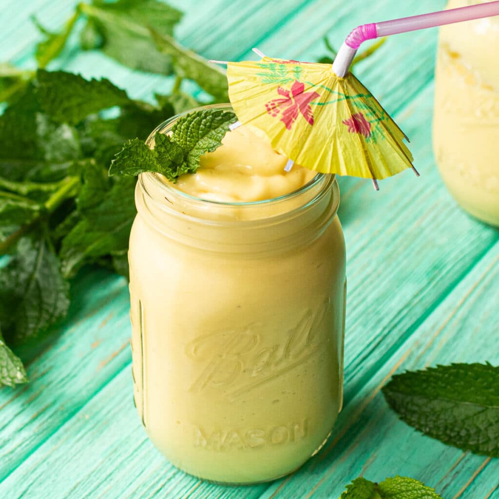 mango smoothie with an umbrella straw, garnished with fresh mint
