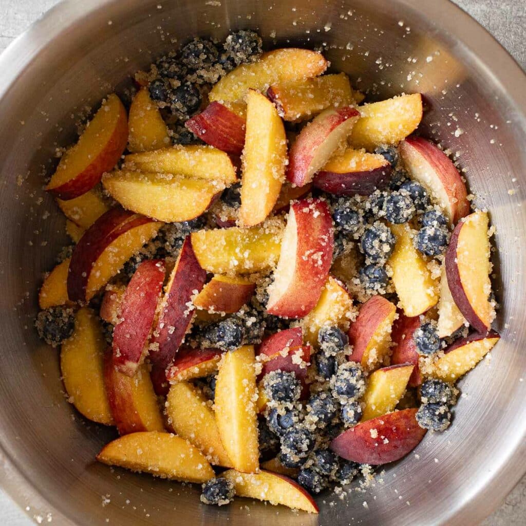 peaches and blueberries mixed with raw sugar in a mixing bowl