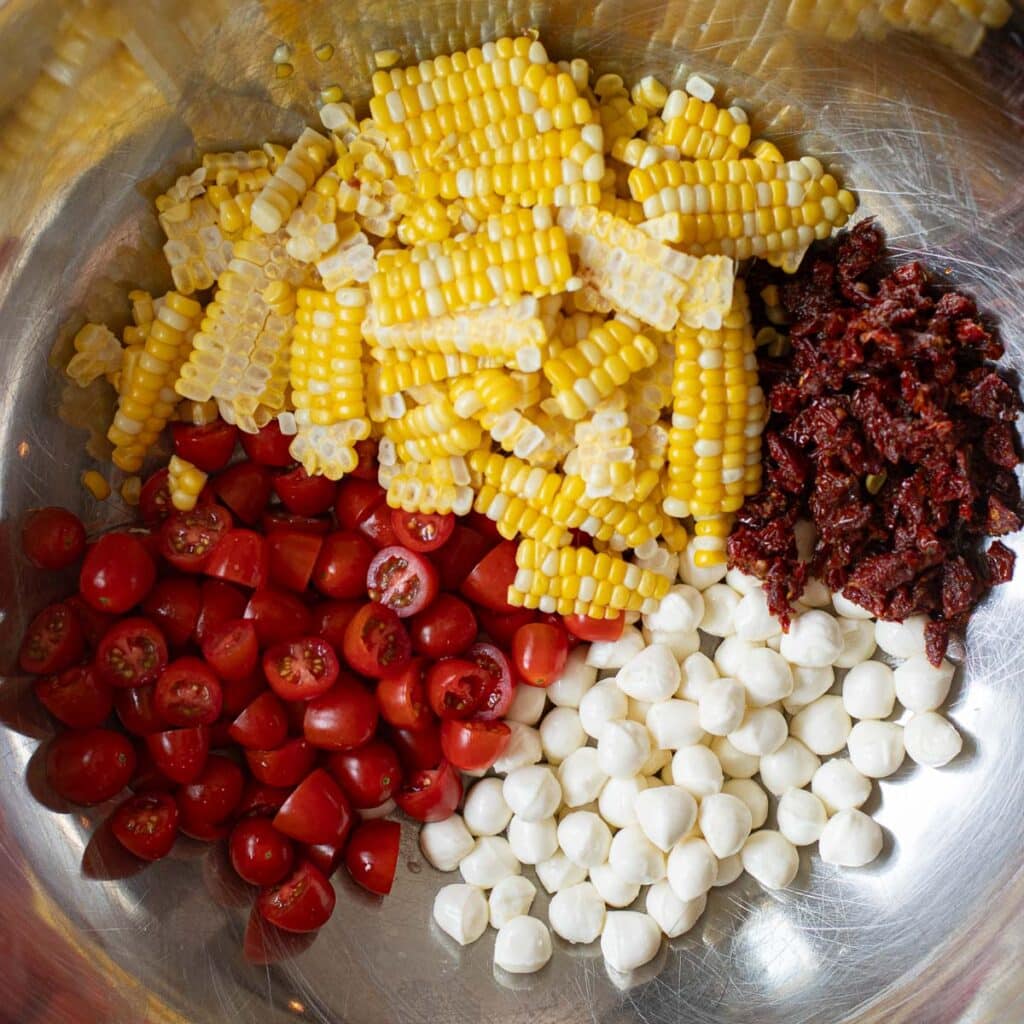 shaved corn, chopped tomatoes, sun dried tomatoes and mozzarella pearls in a large mixing bowl