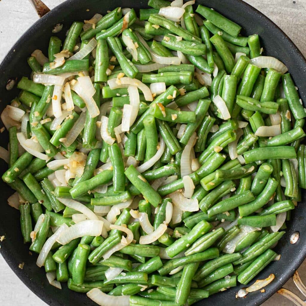 sliced onions and string beans cooking in a pan