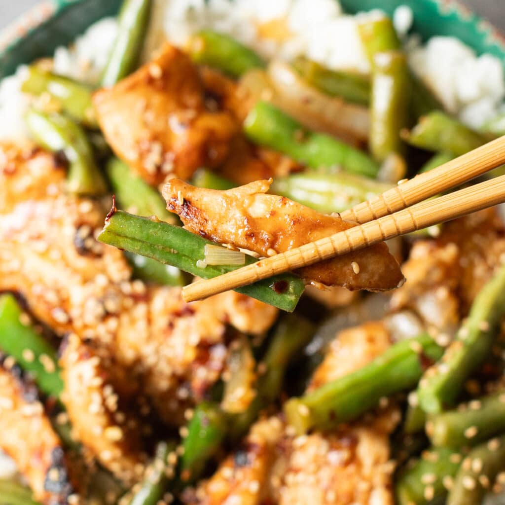 chopsticks holding chicken and string beans