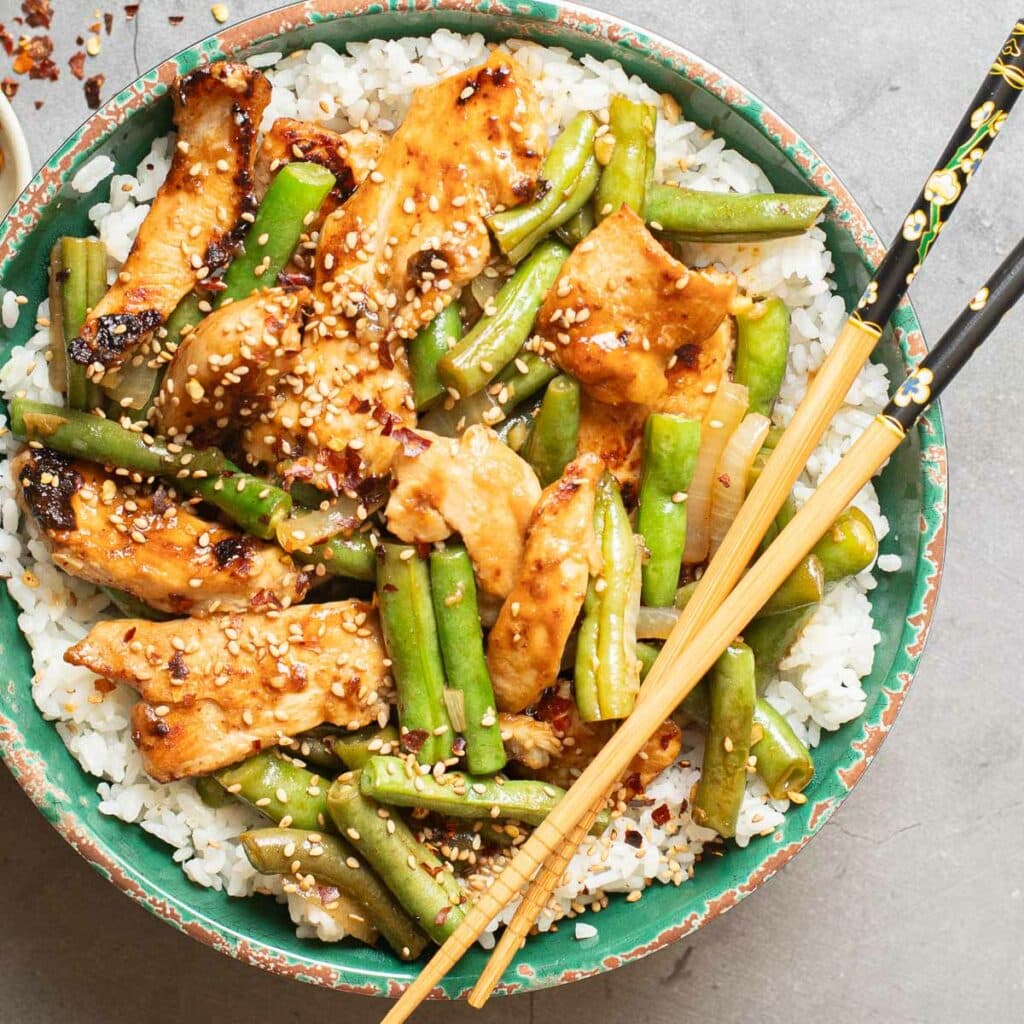 String Bean Chicken over white rice in a green bowl with chopsticks