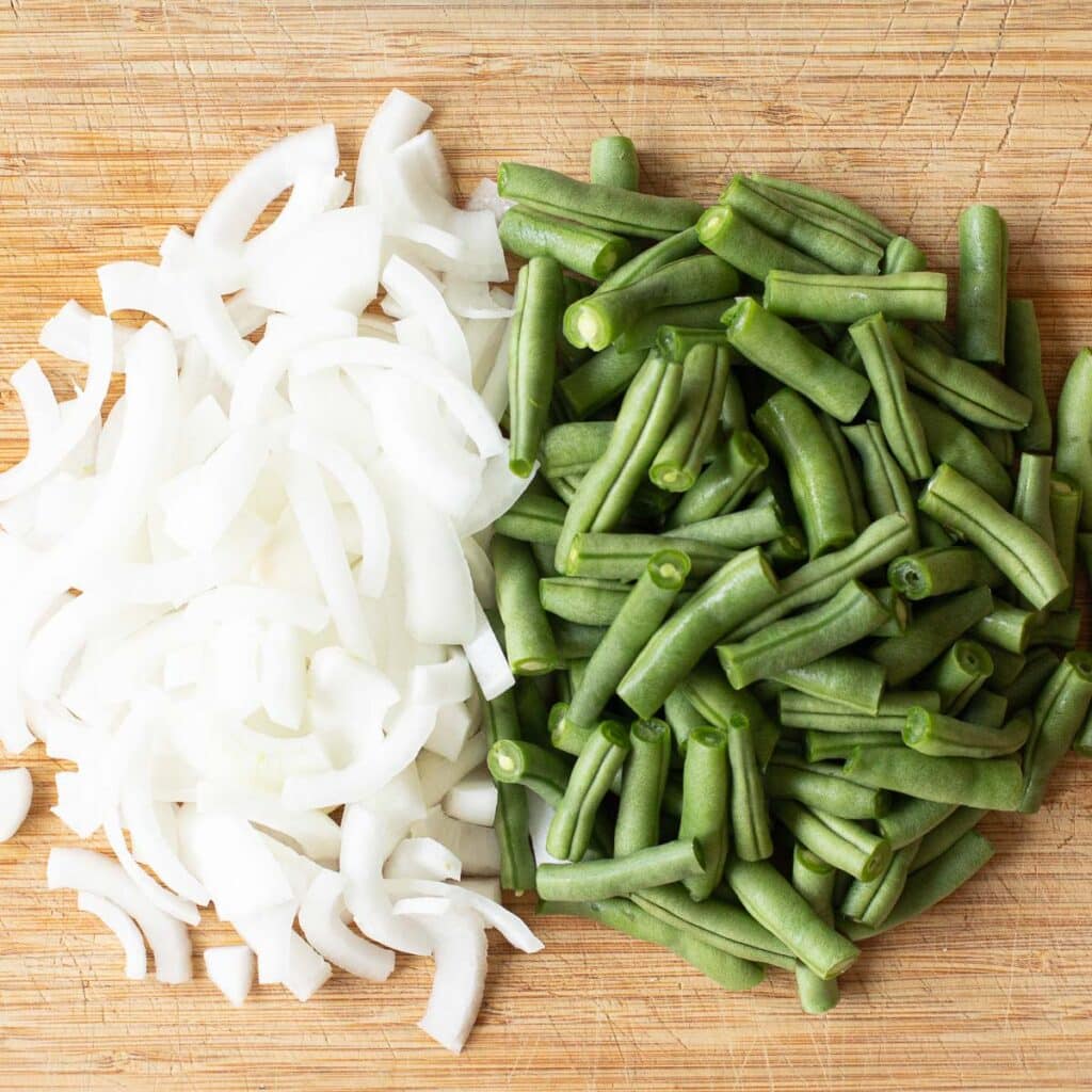 sliced onion and string beans on a wooden cutting board