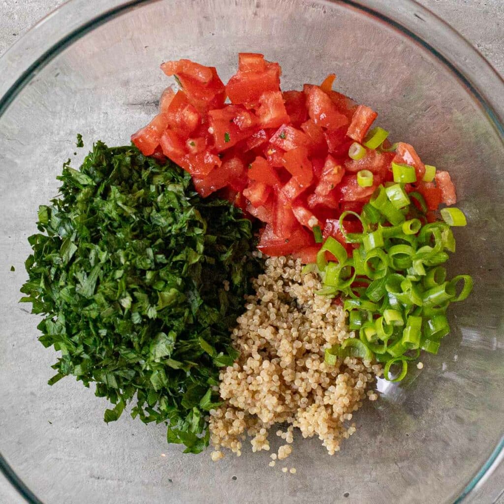 chopped tomatoes, chopped parsley, chopped green onions and quinoa in a glass mixing bowl
